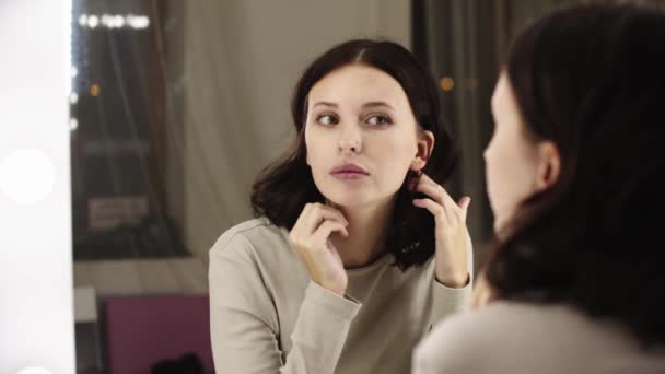 Jovem mulher bonita sentada na frente de um espelho e fixando seu cabelo — Vídeo de Stock