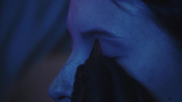 Mężczyzna makijaż artysta wyrywa włosy swoich klientek brwi w ciemnoniebieskim oświetleniu — Wideo stockowe