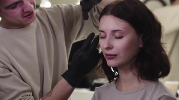 Makyaj sanatçısı, stüdyodaki güzel bayan müşterisinin kaş kıllarına ağda yapıyor. — Stok video