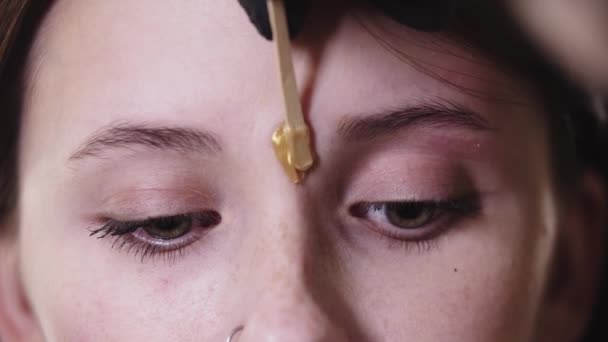 Aplicando cera entre as sobrancelhas em uma mulher bonita — Vídeo de Stock