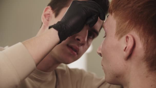 Un maître sourcil homme épilant les poils du sourcil de son client — Video