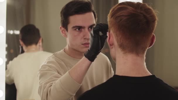 Майстер брів чоловіка, який працює з бровами свого клієнта - вид з дзеркала — стокове відео