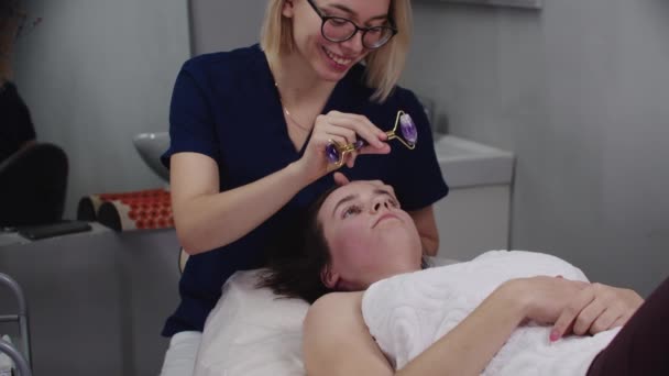 Mujer masajista mostrando diferentes rodillos faciales a su cliente femenino antes de comenzar el procedimiento — Vídeo de stock