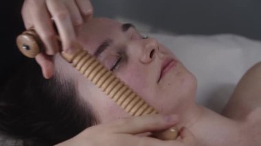 Kadın masajcı, kadın müşterisinin yanağına tahta tırtıklı bir alet kullanıyor.