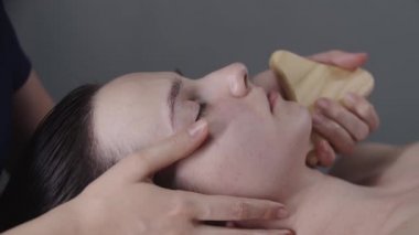Kadın masajcı kadın müşterisinin çenesinin altında ahşap bir alet kullanıyor.