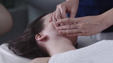 Kadın masajcı kadın müşterisine parmaklarını kullanarak yüz masajı yapıyor.