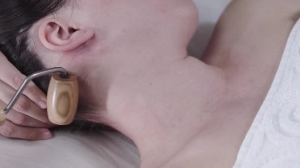 Massageassistentin mit einer Holzrolle am Hals ihrer Kundin — Stockvideo