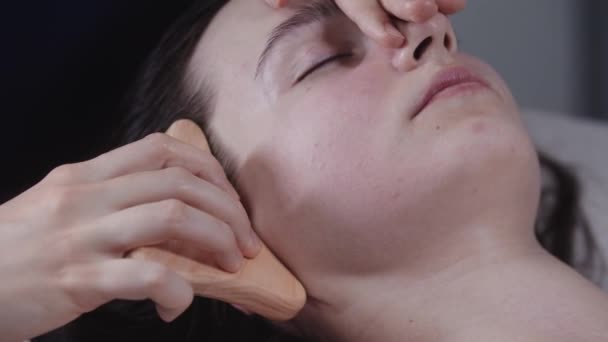 ผิวหนังของผู้หญิงนวดเรียบเนียนโดยใช้เครื่องมือไม้บนแก้มของลูกค้าหญิงของเธอ — วีดีโอสต็อก