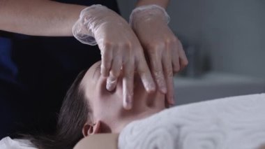 Masajcı, kadın müşterisine parmaklarını kullanarak yüz masajı yapıyor.