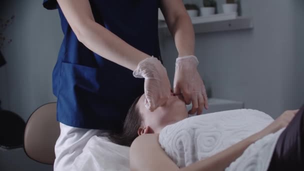 Массажист-блондинка делает массаж лица пальцами на клиентке — стоковое видео