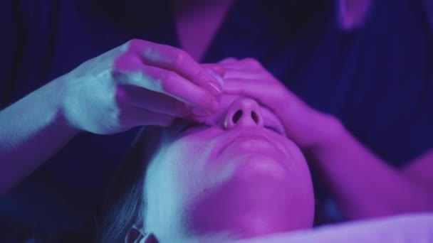 ブロンド若い女性マッサージをしている彼女の女性のクライアント上の玉片を使用して顔-ネオン照明 — ストック動画