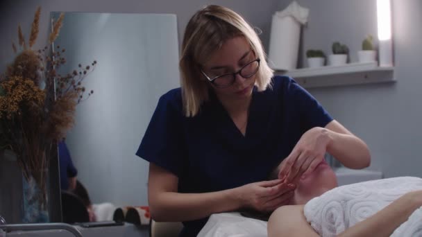 Rubia joven masajista haciendo un masaje facial usando sus dedos en su cliente femenino — Vídeo de stock