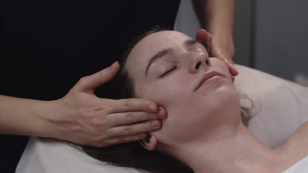Массажист делает массаж лица пальцами на коже своей клиентки — стоковое видео