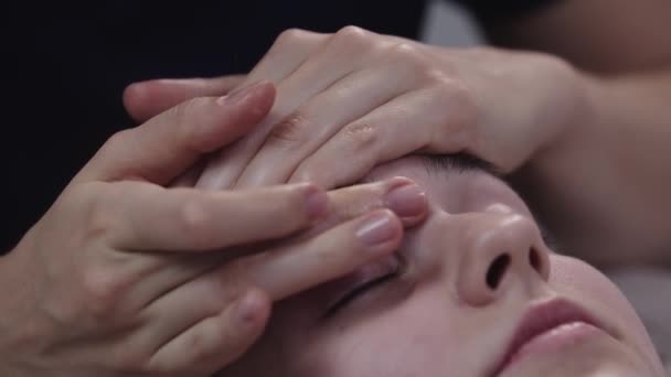マッサージを行うマッサージ彼女の女性のクライアントの皮膚の上に指を使用して – 額の下にマッサージ — ストック動画