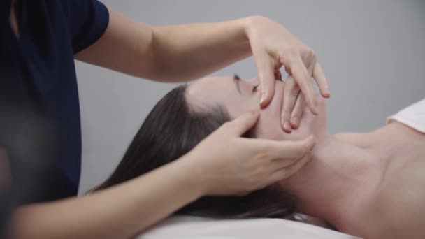 Masajista haciendo un masaje facial usando sus dedos en la piel limpia de su cliente femenino — Vídeo de stock