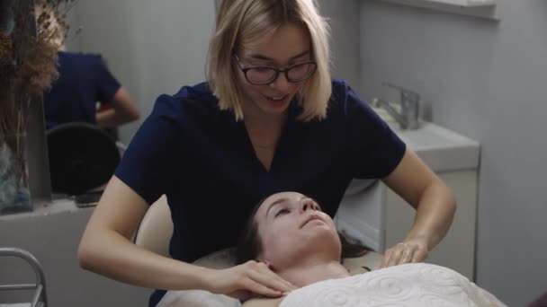 Νεαρή γυναίκα μασέρ καθαρίζει το δέρμα της πελάτισσάς της μετά την επέμβαση — Αρχείο Βίντεο