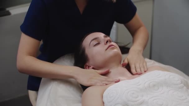 Γυναικείο μασάζ με κρέμα στο λαιμό και το πρόσωπο της πελάτισσάς της μετά τη διαδικασία μασάζ — Αρχείο Βίντεο
