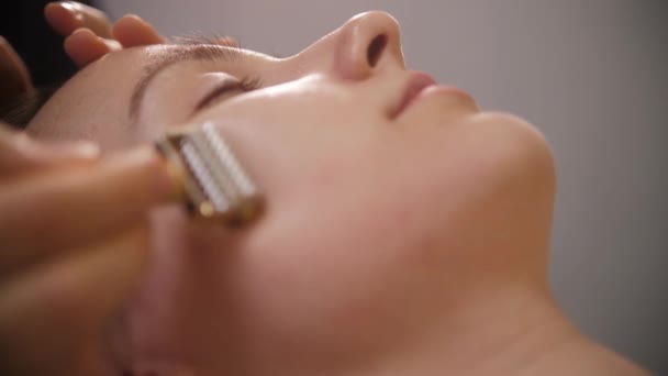 Gezichtsmassage - de massagist met behulp van een spiky roller op de wang van haar vrouwelijke cliënt — Stockvideo