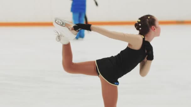 Little girl skater in black and yellow costume spinning on the public ice rink — Stock Video