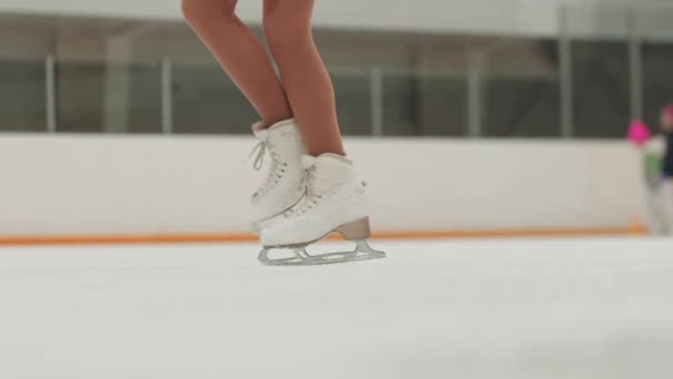 Feche os patins de gelo enquanto executa figura girando na pista de gelo — Vídeo de Stock
