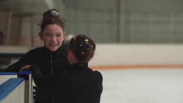 Két kis mosolygós lány műkorcsolyázik a nyilvános jégpálya kapujában és beszélgetnek. — Stock videók