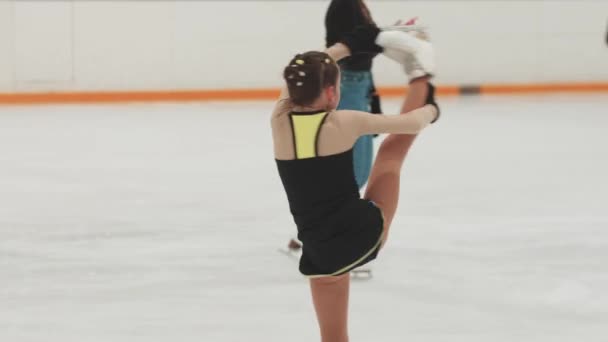 Menina figura patinadora em preto e amarelo traje de treinamento girando em torno da pista pública — Vídeo de Stock