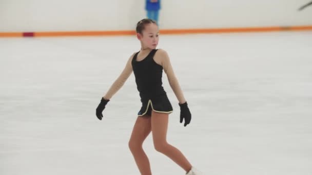 Klein meisje kunstschaatser in opleiding zwart en geel kostuum schaatsen op de openbare ijsbaan — Stockvideo