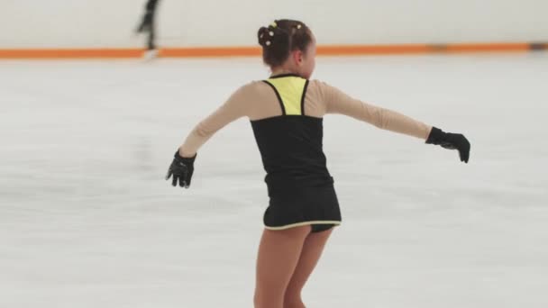 Ragazza pattinatrice di figura in formazione nero e giallo costume pattinaggio sulla pista di pattinaggio pubblico e cadere — Video Stock