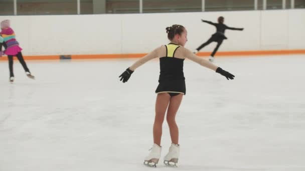 Mała dziewczynka łyżwiarz figurowy w treningu czarny i żółty kostium łyżwiarstwo na lodowisku i upadek po spin — Wideo stockowe