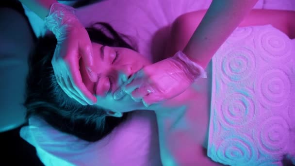 Massage session - ung kvinna massera ansiktet på sin kvinnliga klient i lila belysning — Stockvideo