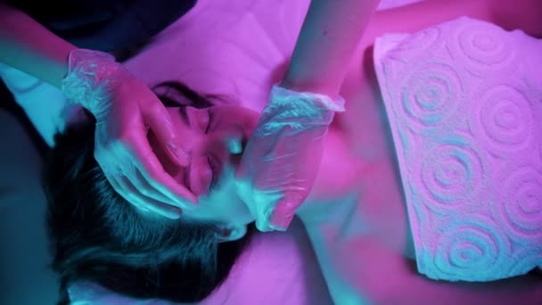 Massage session - ung kvinna massera ansiktet på sin kvinnliga klient i neon lila belysning — Stockvideo