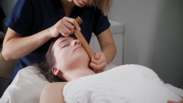 Masáž obličeje - terapeutka pomocí velkého žebrovaného dřevěného nástroje na tváři své klientky — Stock video