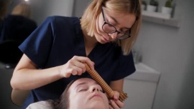 Yüz masajı - kadın bir terapist kadın müşterisinin yüzüne büyük tahta bir alet kullanıyor.