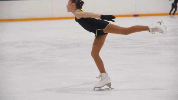 Een klein meisje traint haar kunstschaatsen op de openbare schaatsbaan - ze draait ter plekke. — Stockvideo