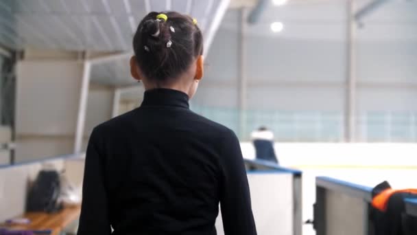 Uma garota patinadora artística caminha até os portões da pista de gelo pública e está prestes a ir para o gelo — Vídeo de Stock