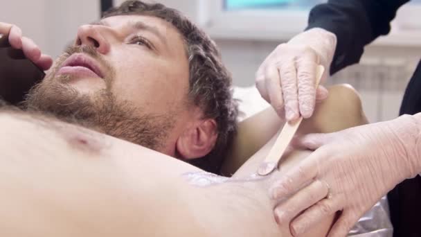 El maestro de la depilación tirando de la piel en la axila masculina y aplicando cera caliente con una espátula — Vídeo de stock