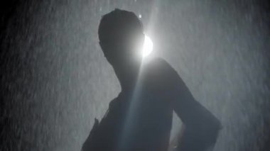 Güzel vücutlu, yağmurun altında dans eden, ıslak tişörtlü seksi genç bir kadın.