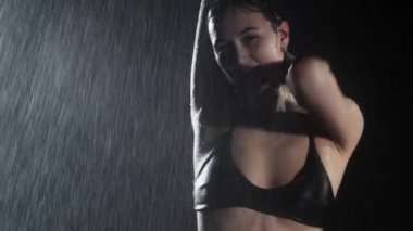Çekici ve gülümseyen genç bir kadın seksi zayıf vücutlu, yağmurun altında dans eden.