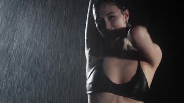 Çekici ve gülümseyen genç bir kadın seksi zayıf vücutlu, yağmurun altında dans eden. — Stok video