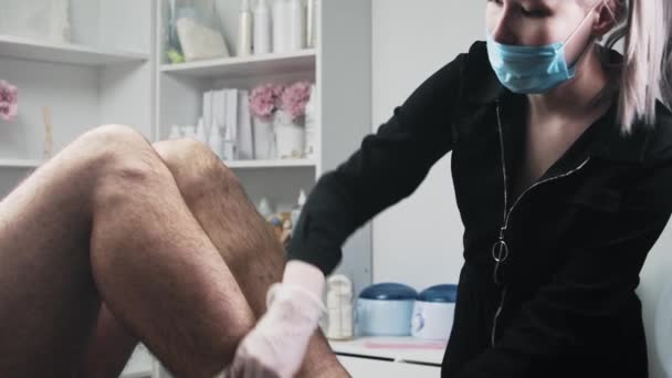 Waxing procedure - Epilationsmeisterin bereitet das Bein ihres männlichen Klienten auf das Wachsen vor — Stockvideo