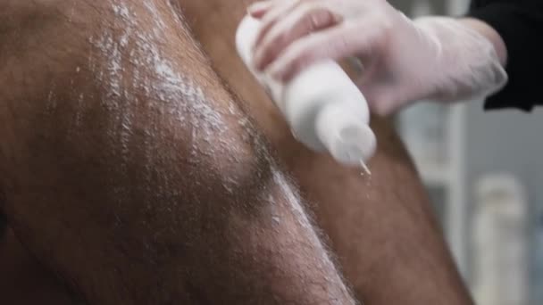 Procédure d'épilation - maître épilation appliquant de la poudre de talc sur la jambe de son client masculin — Video