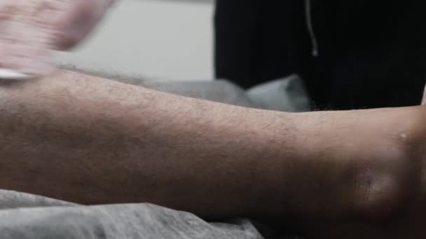 Procedura woskowania - mistrz depilacji rozmazujący talk na nodze jej męskiego klienta — Wideo stockowe