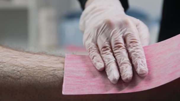 Procedimento de depilação - o mestre esfrega a tira na perna de seu cliente — Vídeo de Stock