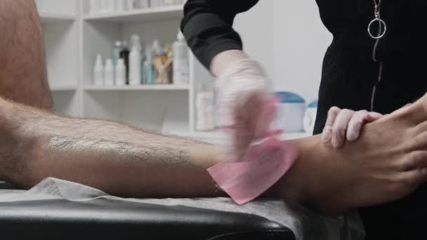 Procedimiento de depilación: el maestro de depilación frota la tira en la pierna de su cliente y rasga los pelos — Vídeo de stock