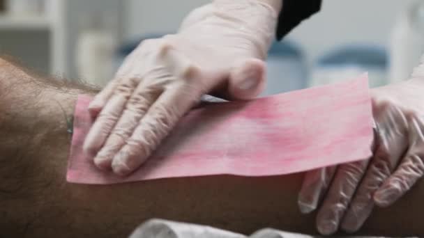 Procedimento de depilação - o mestre esfrega a tira na perna de seu cliente e rasga os cabelos na perna — Vídeo de Stock