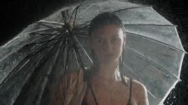 Yağmurun altında elinde şemsiyeyle bekleyen genç ve seksi bir kadın. — Stok video