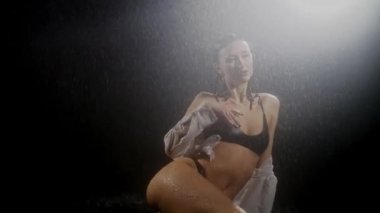 Seksi vücutlu genç bir kadın yağmur altında çekim yapıyor sahne arkasında çekim yapıyor.