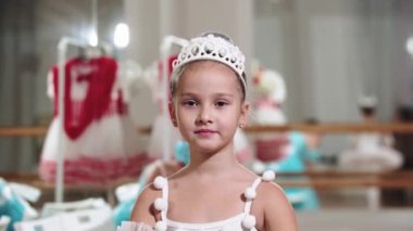 Küpeli, gülümseyen küçük balerin kız kameraya bakıyor.