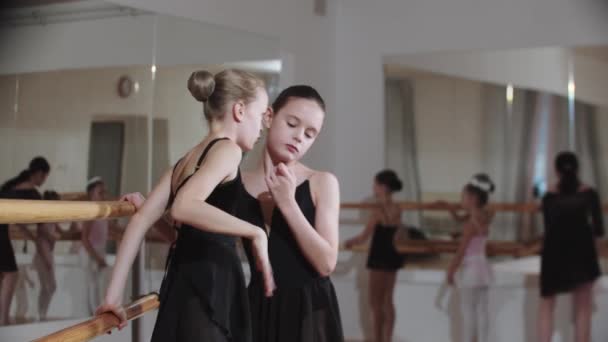 Дві маленькі дівчата щось шепочуть один одному біля підставки балетної студії — стокове відео