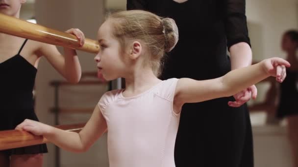 Две девушки-балерины тренируются в студии возле стенда с помощью тренера-женщины — стоковое видео